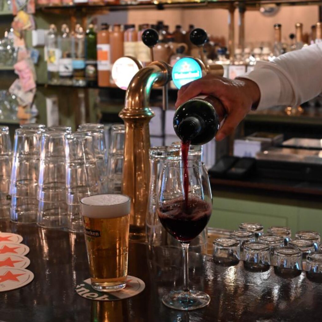 Rode wijn wordt ingeschonken in een glas op een bar, naast een Heineken bier en taps.