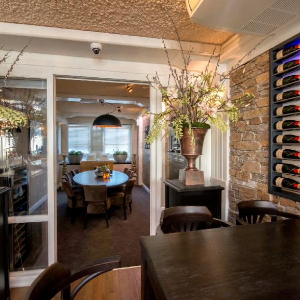 Restaurant interieur met stenen muur, blauw verlicht wijnenrek vol Moët & Chandon en doorkijk naar eetzaal.