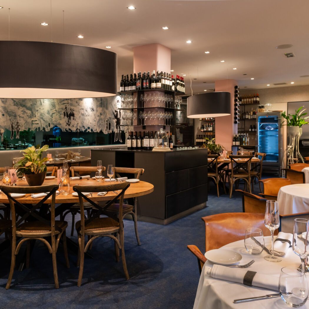 Stijlvol restaurantinterieur met gedekte tafels, houten en lederen stoelen, en een uitgebreide wijnbar.