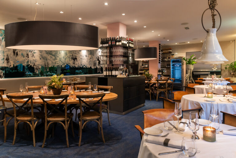 Stijlvol restaurantinterieur met gedekte tafels, houten en lederen stoelen, en een uitgebreide wijnbar.