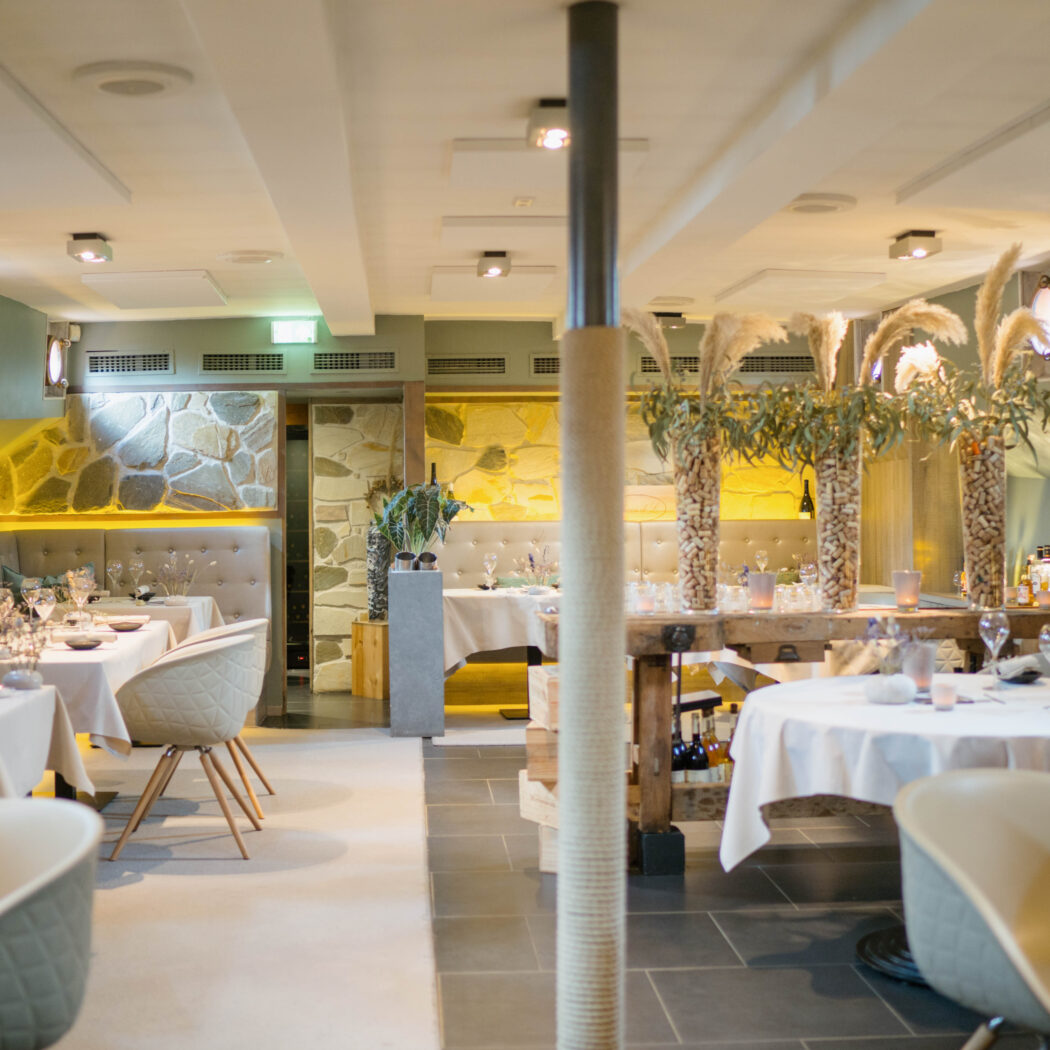 Elegant restaurant interieur met gedekte tafels, stenen muur, en sfeervolle decoratie van pampasgras en wijnkurken.