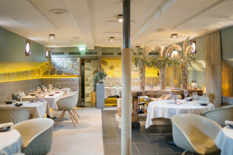 Elegant restaurant interieur met gedekte tafels, stenen muur, en sfeervolle decoratie van pampasgras en wijnkurken.