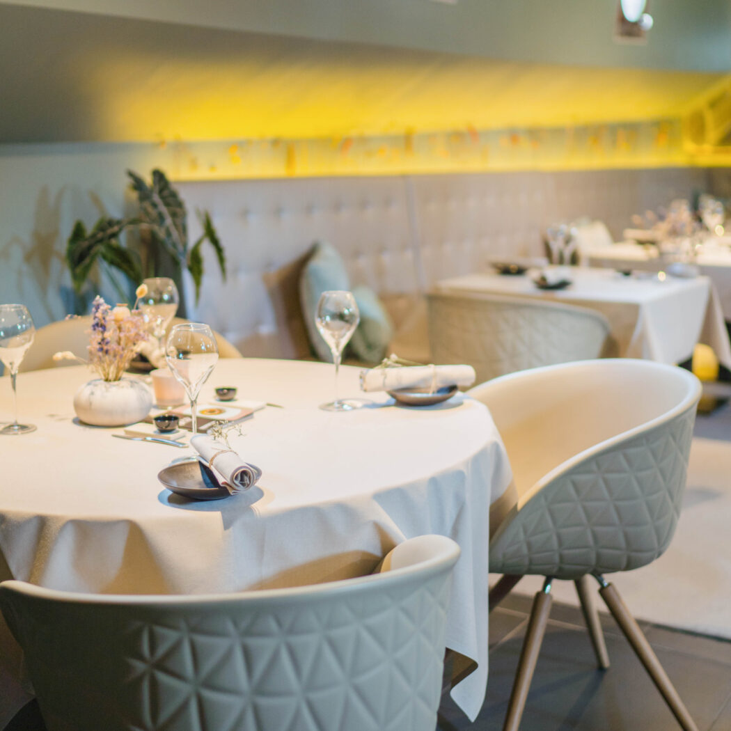Stijlvol restaurant interieur met gedekte tafels, moderne beige stoelen en bloemdecoratie.