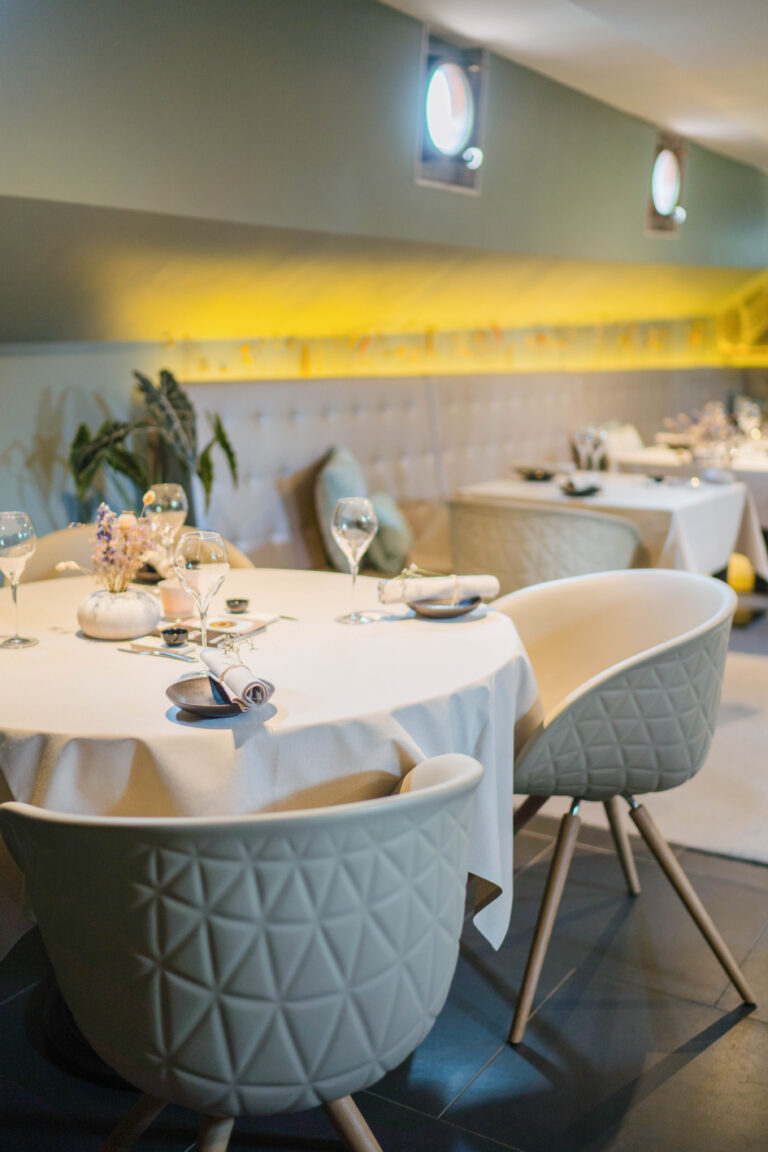 Stijlvol restaurant interieur met gedekte tafels, moderne beige stoelen en bloemdecoratie.