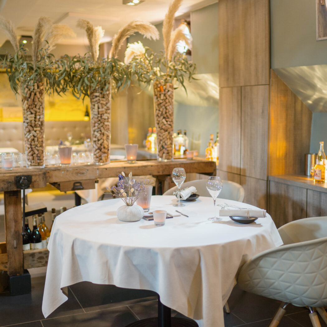 Ronde restauranttafel gedekt voor twee met wijnglazen, bloemen en kaarslicht in een modern interieur.