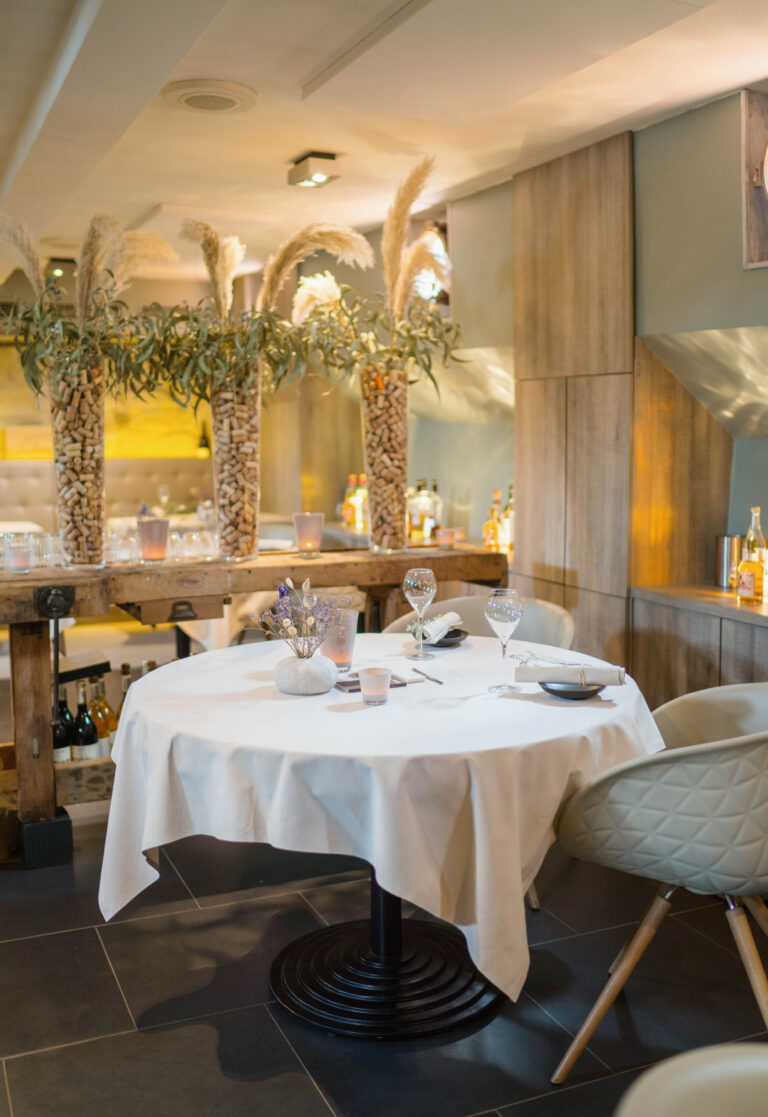 Ronde restauranttafel gedekt voor twee met wijnglazen, bloemen en kaarslicht in een modern interieur.