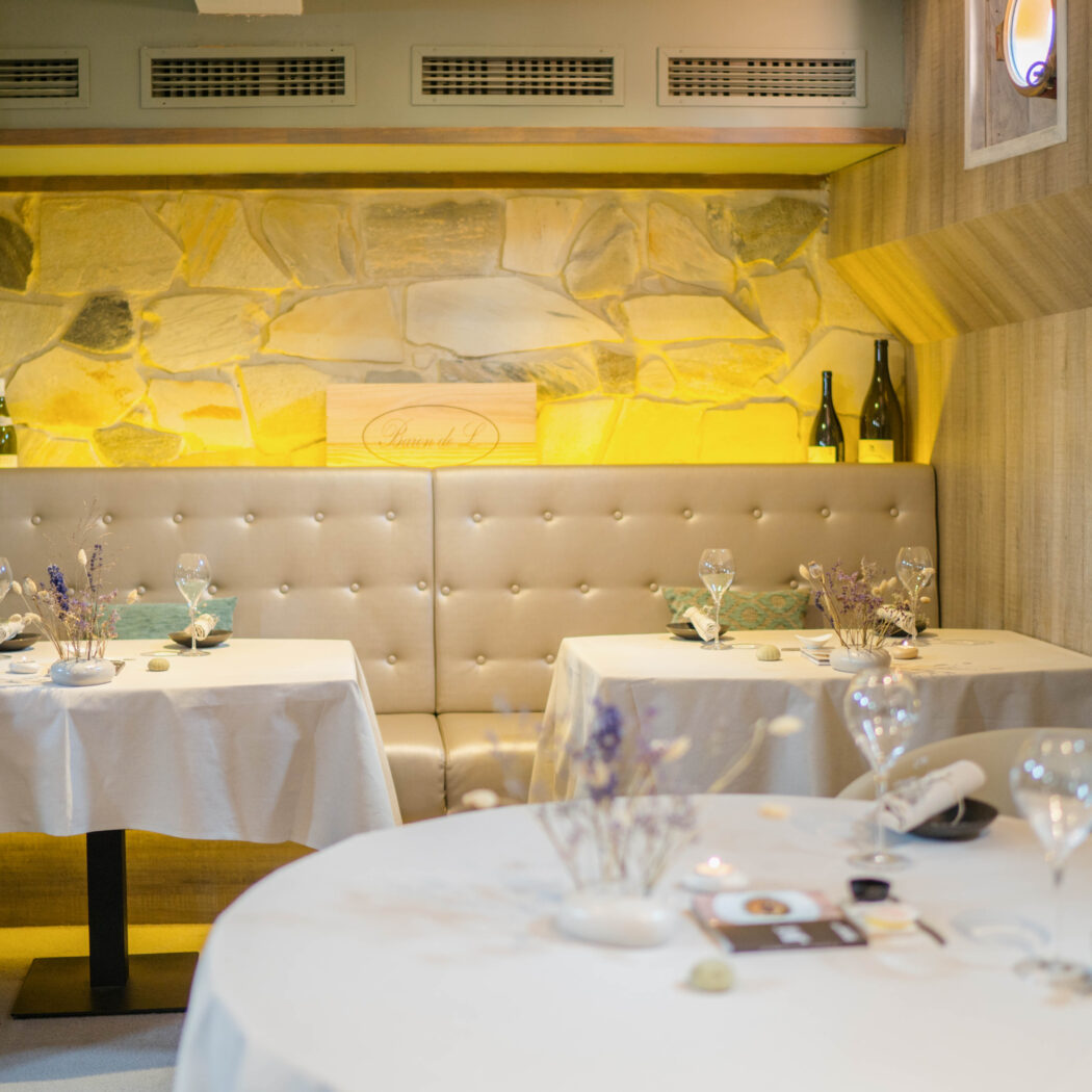 Sfeervolle restaurantinrichting met gedekte tafels, een lichte bank en een stenen muur met achtergrondverlichting.