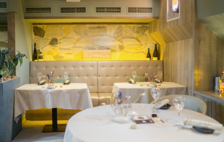 Sfeervolle restaurantinrichting met gedekte tafels, een lichte bank en een stenen muur met achtergrondverlichting.