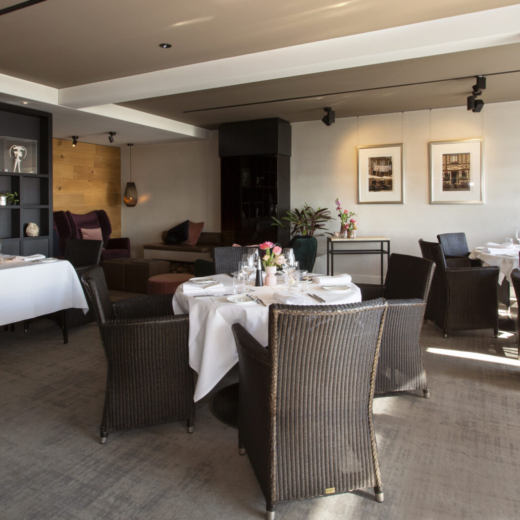 Elegante restaurantzaal met wit gedekte tafels, rieten stoelen, houten wand en Michelin 2021 award.