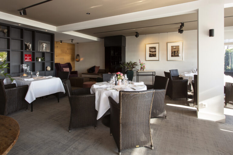 Elegante restaurantzaal met wit gedekte tafels, rieten stoelen, houten wand en Michelin 2021 award.