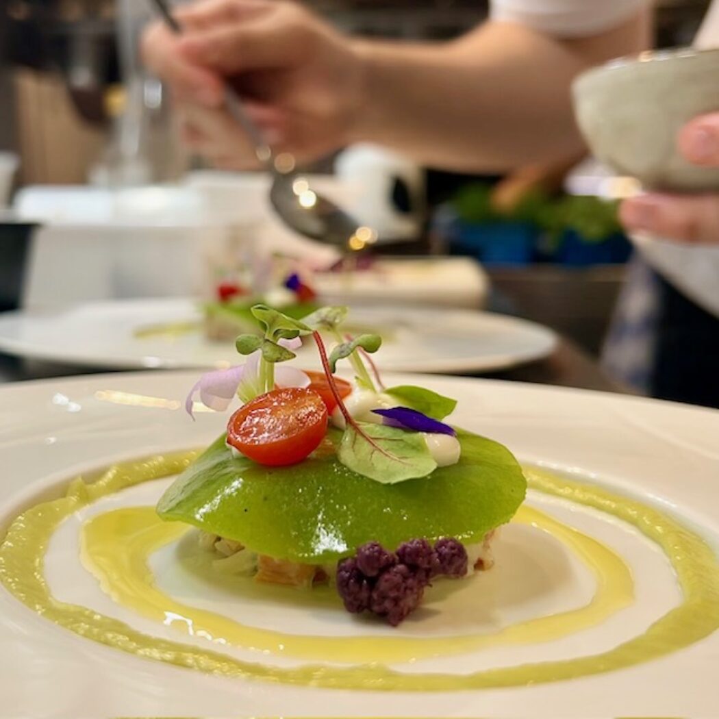 Verfijnd gerecht met heldergroene laag, cherrytomaat, eetbare bloemen en gele saus, opgemaakt door een chef.