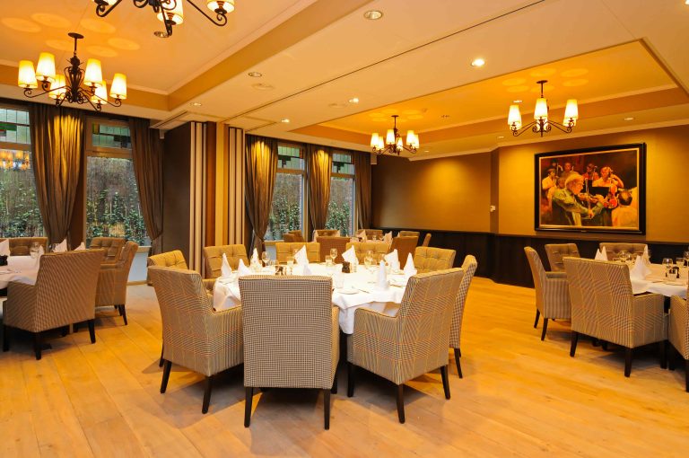 Sfeervolle restaurantzaal met gedekte ronde tafels, beige gestoffeerde stoelen en een groot schilderij aan de muur.
