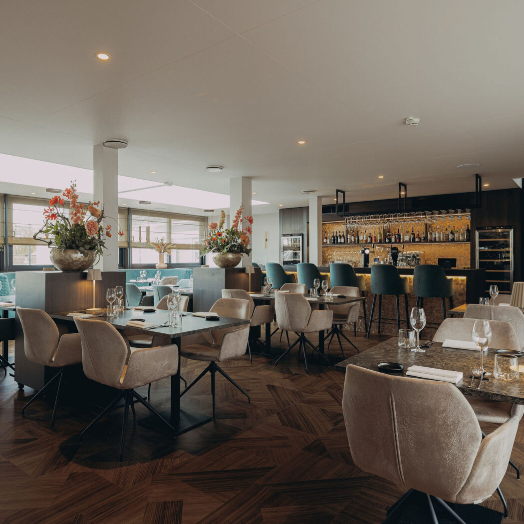 Elegant restaurant interieur met donkere tafels, beige stoelen, een bar met teal krukken en een geometrische houten vloer.