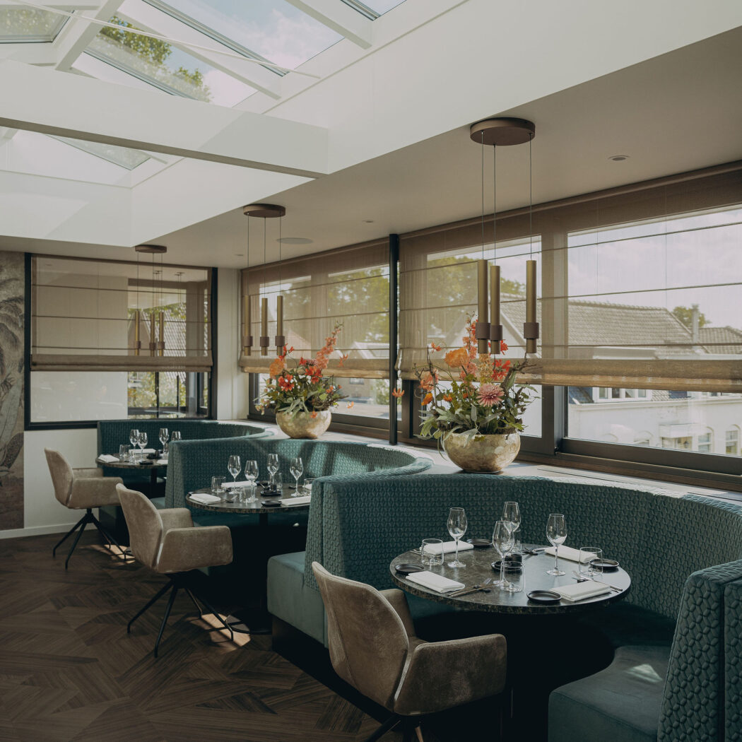 Modern restaurant interieur met teal gebogen banken, gedekte marmeren tafels, beige stoelen en een glazen dak.
