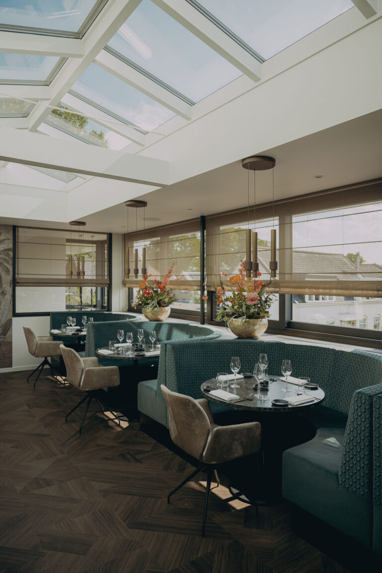 Modern restaurant interieur met teal gebogen banken, gedekte marmeren tafels, beige stoelen en een glazen dak.