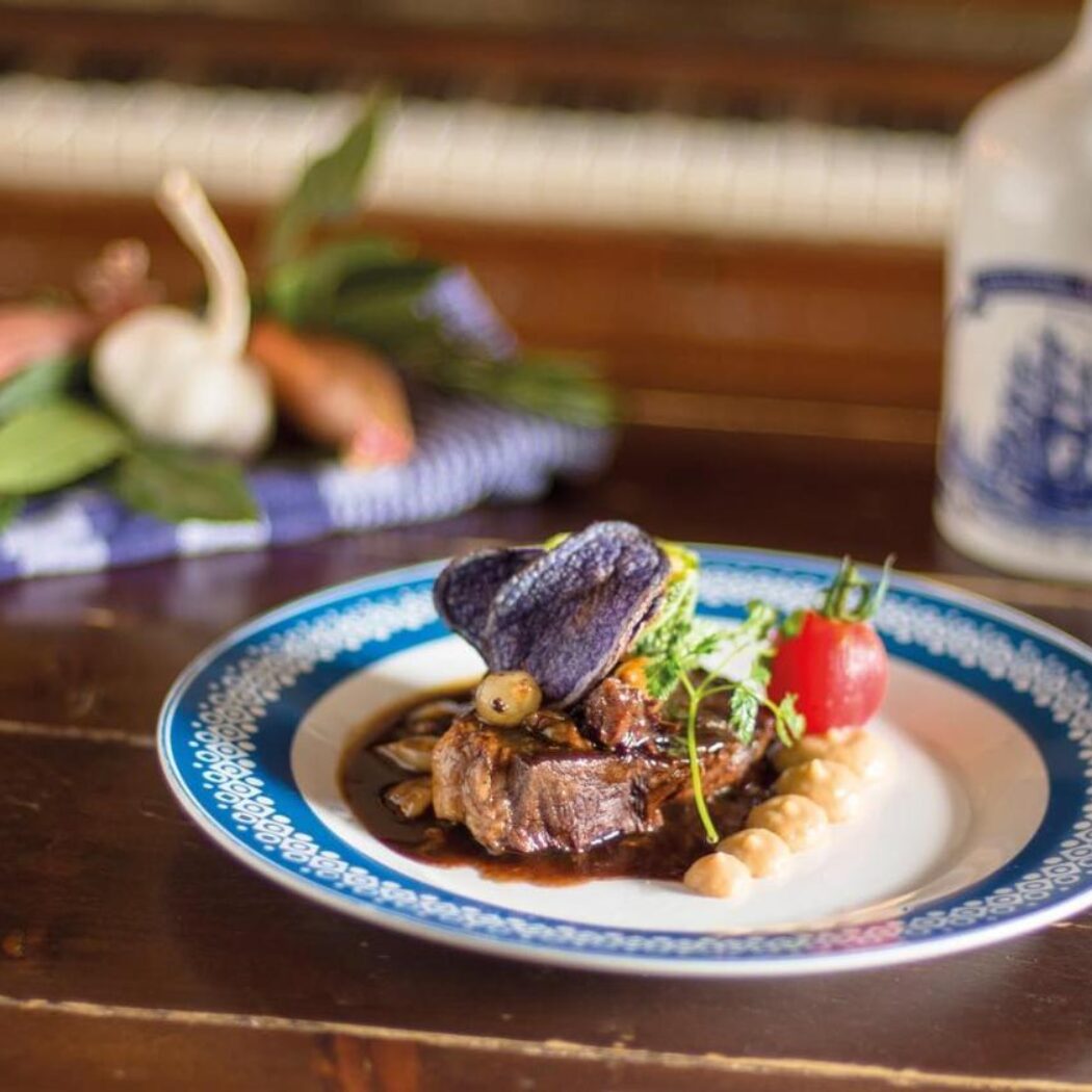 Elegant stoofvleesgerecht met paarse hartchip, tomaat en puree op een bord met Delfts blauw patroon.