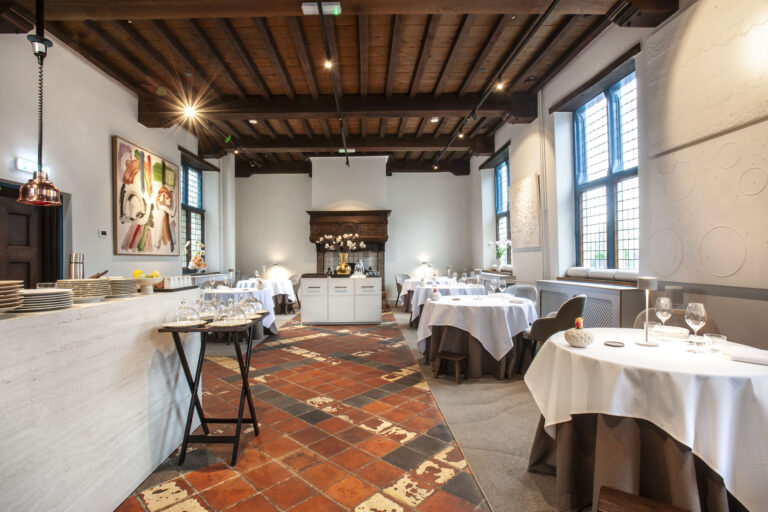 Elegant restaurant interieur met wit gedekte tafels, houten balkenplafond en antieke terracotta vloertegels.