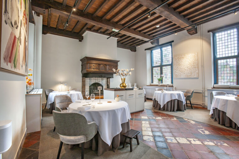 Sfeervol restaurantinterieur met gedekte tafels, een decoratieve open haard en houten balkenplafond.
