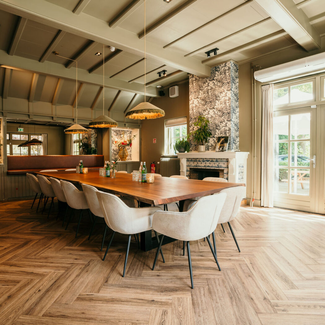 Sfeervolle privé eetzaal in groentinten met lange houten tafel, lichte stoelen, visgraatvloer en tuinzicht.