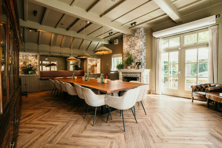 Sfeervolle privé eetzaal in groentinten met lange houten tafel, lichte stoelen, visgraatvloer en tuinzicht.