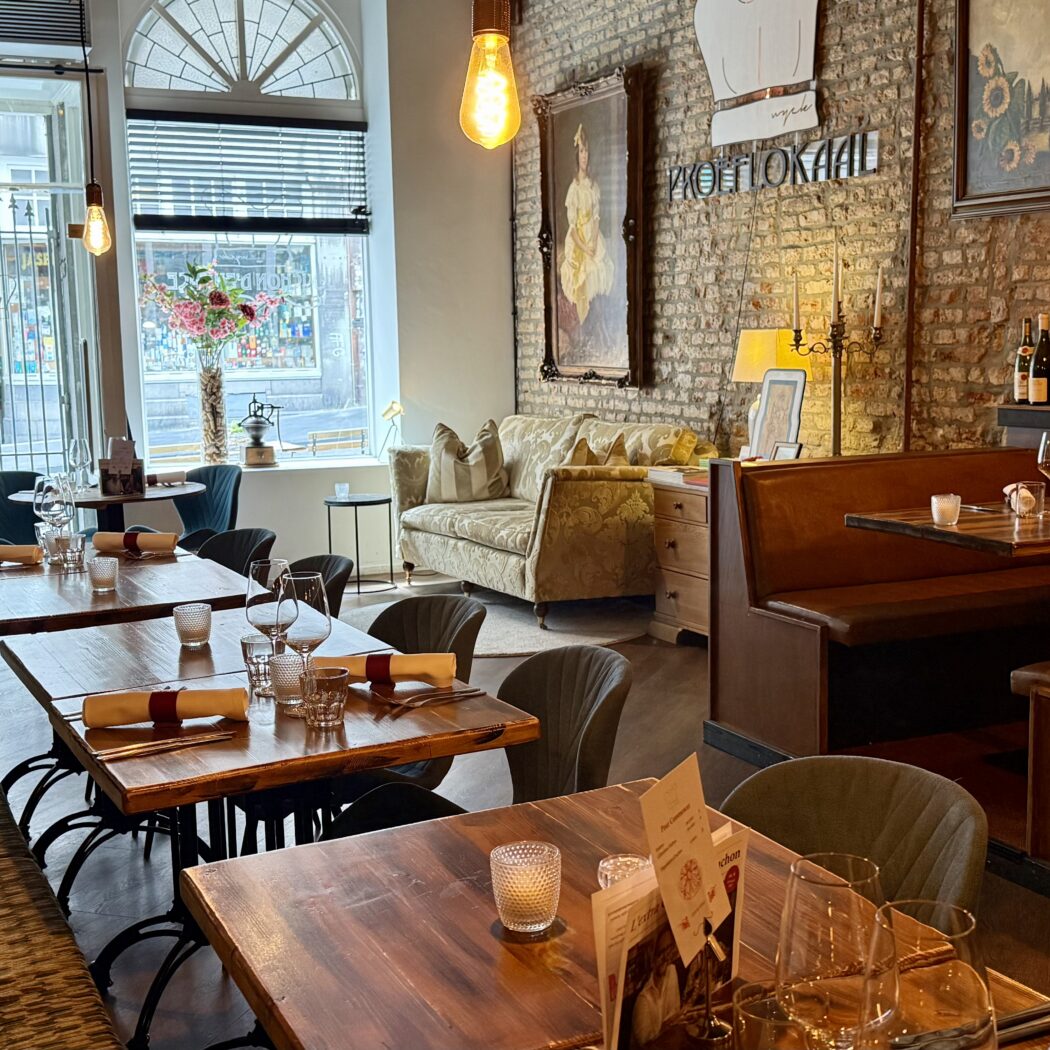 Restaurantinterieur: houten tafels, lederen banken,  schilderijen en wijnrek.