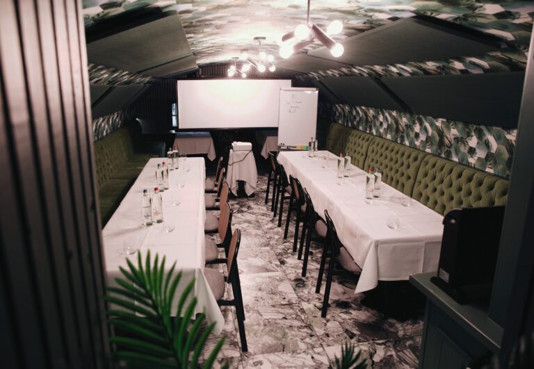 Stijlvolle vergaderzaal met lange tafels, groene banken, projectiescherm en bladmotief plafond.