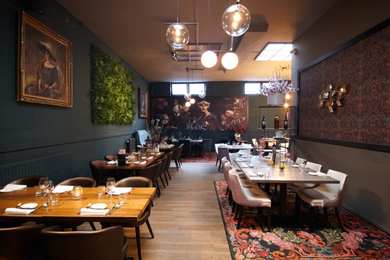 Sfeervol restaurantinterieur met donkere muren, houten tafels en kunstzinnige decoraties.