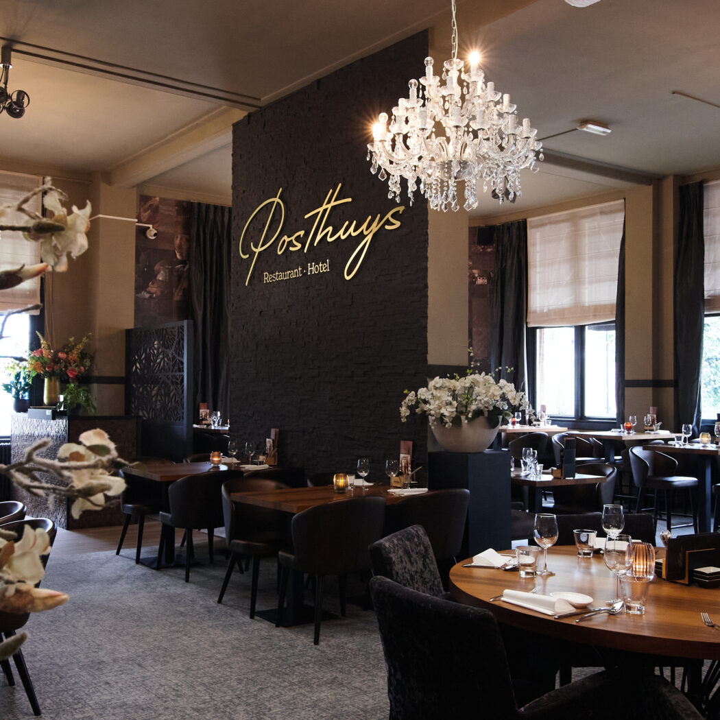 Restaurant Posthuys Hotel met luxe gedekte tafels, kristallen kroonluchters en gouden naamschild op donkere muur.