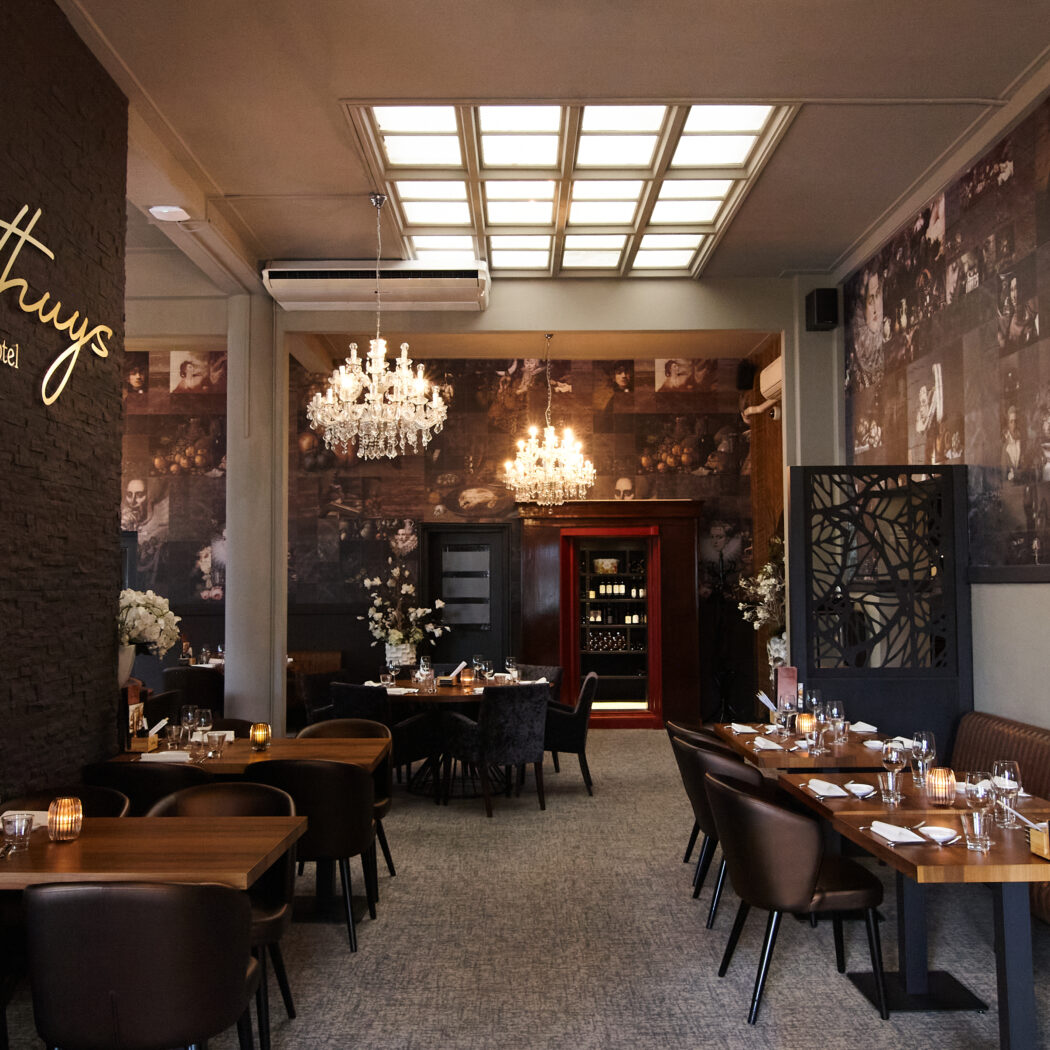 Elegant interieur van Posthuys Restaurant Hotel met gedekte tafels, leren zitplaatsen en muren vol klassieke portretten, verlicht door kroonluchters.