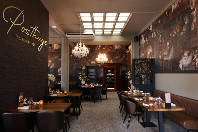 Elegant interieur van Posthuys Restaurant Hotel met gedekte tafels, leren zitplaatsen en muren vol klassieke portretten, verlicht door kroonluchters.