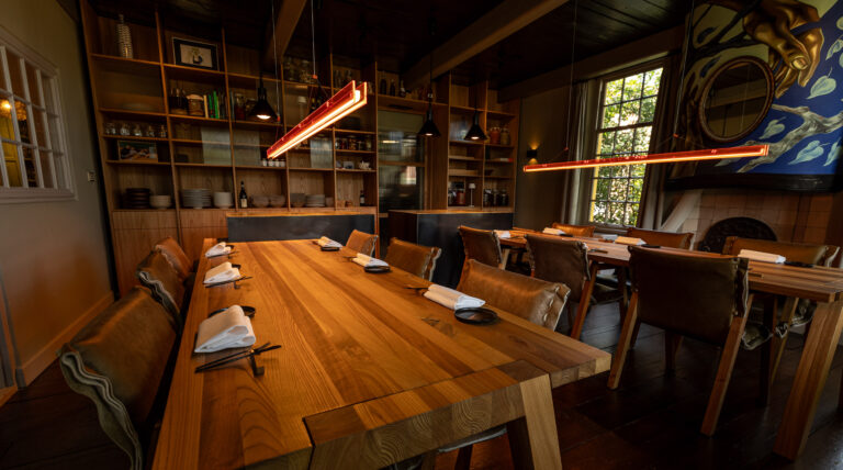 Sfeervolle eetzaal met lange eikenhouten tafels en leren stoelen, verlicht door moderne rode hanglampen.