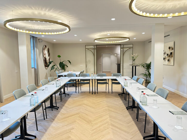 Stijlvolle vergaderruimte met U-vormige tafelopstelling, voorbereid met waterflessen en glazen, onder moderne ringlampen.