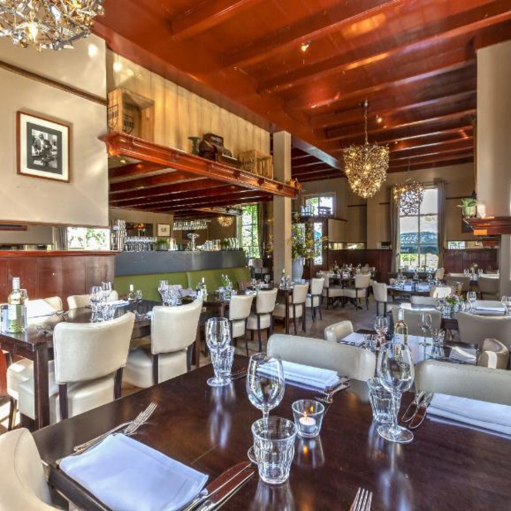 Warm en elegant restaurantinterieur met gedekte tafels, houten balken en kroonluchters.