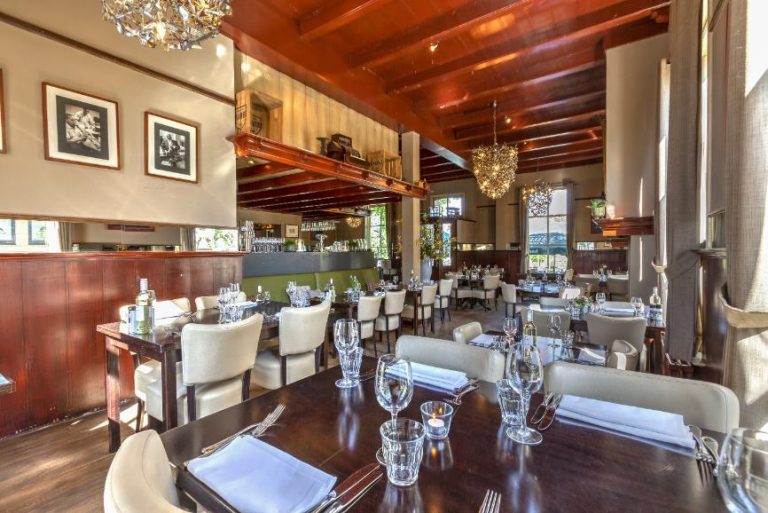 Warm en elegant restaurantinterieur met gedekte tafels, houten balken en kroonluchters.