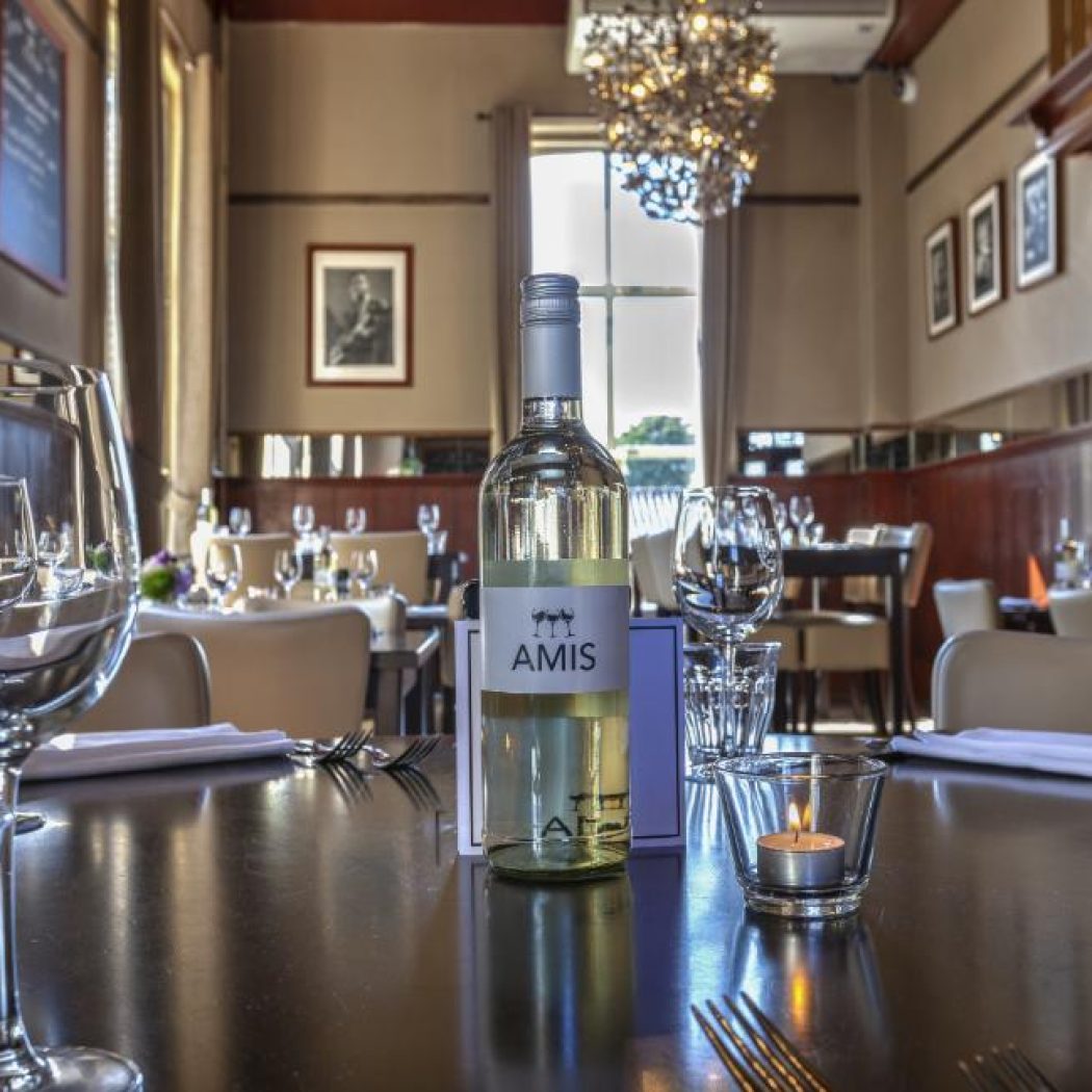 Witte wijnfles AMIS met wijnglazen en een brandend theelichtje op een donkere houten restauranttafel.