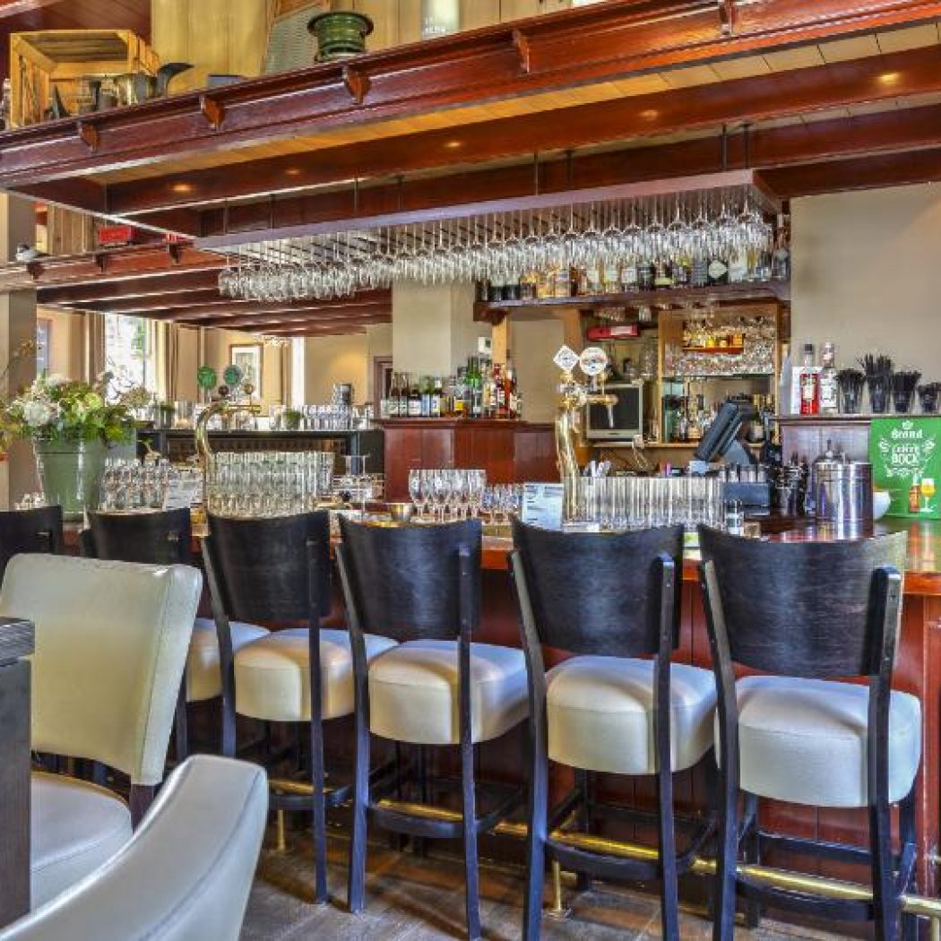 Gezellig interieur van een traditionele bar met houten toonbank, barkrukken, bierkranen en hangende wijnglazen.