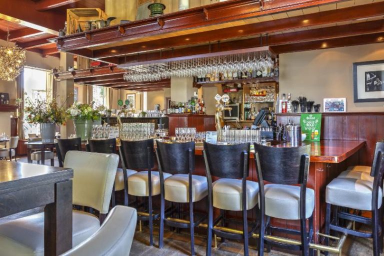 Gezellig interieur van een traditionele bar met houten toonbank, barkrukken, bierkranen en hangende wijnglazen.