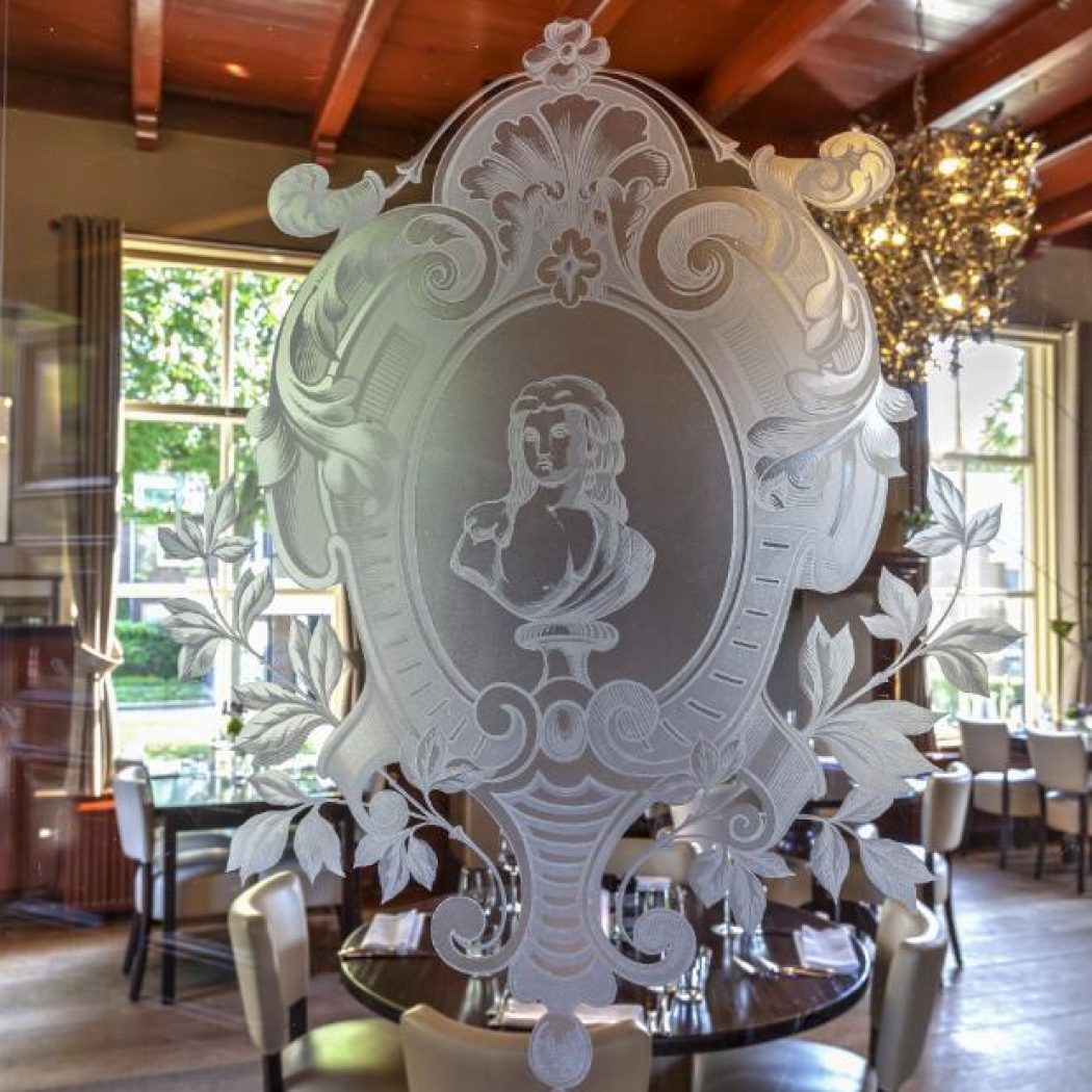 Decoratief geëtst glaspaneel met buste van vrouw en bladmotieven in een klassiek restaurant.