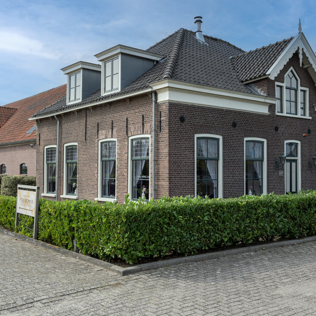 Donker bakstenen gebouw met grijs dak, witte kozijnen, een PAASHAAS TERBORG bord en EV-laadpaal.