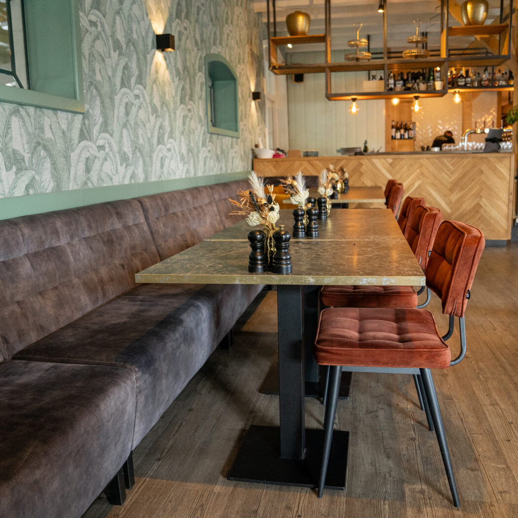 Restaurant interieur met lange bruine fluwelen bank, gouden tafels, oranje fluwelen stoelen en groene tropische muur.