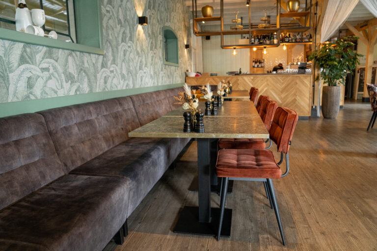 Restaurant interieur met lange bruine fluwelen bank, gouden tafels, oranje fluwelen stoelen en groene tropische muur.