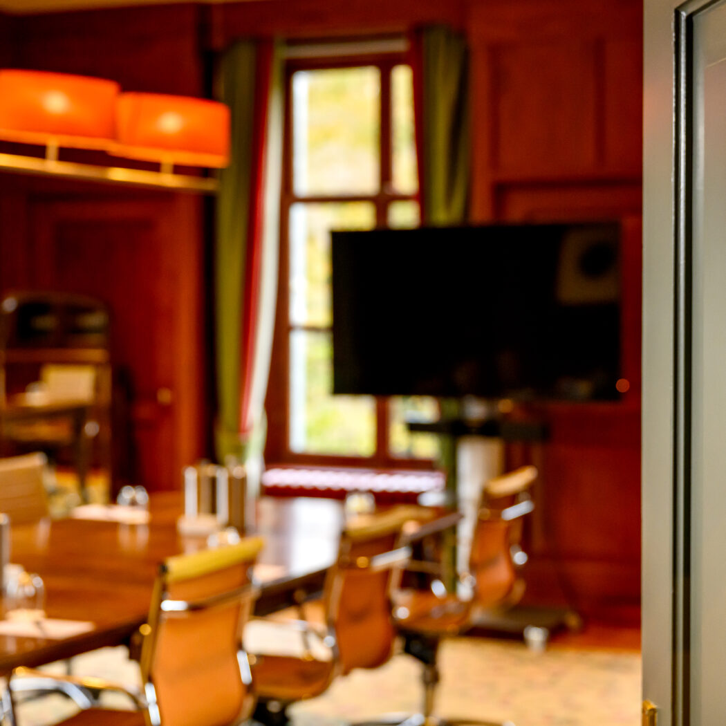 Zicht op een vergaderzaal met lange houten tafel en stoelen, door een open deur met naambordje BENTINCK.