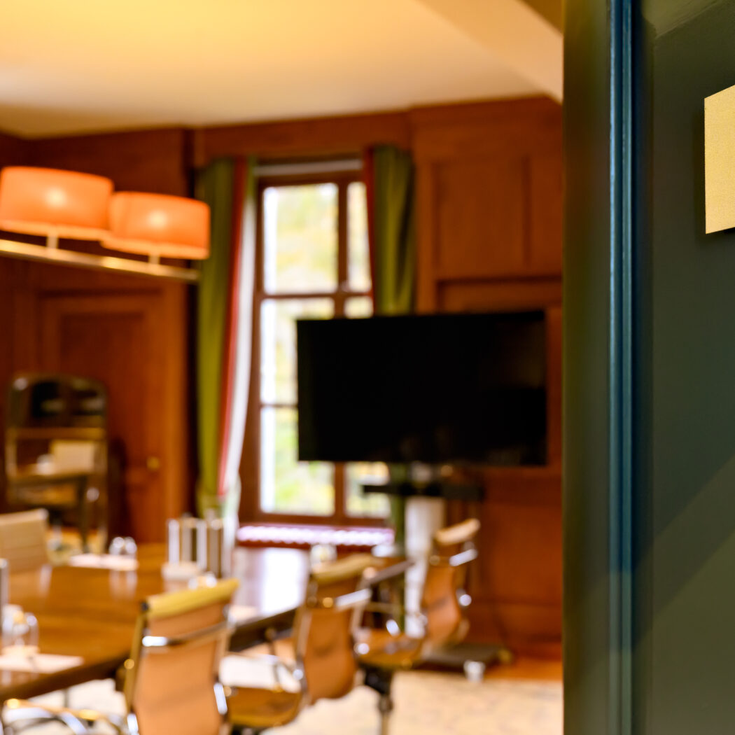 Gouden naambord BENTINCK met een wapen aan een donkergroene muur, met uitzicht op een vergaderzaal met houten tafel en tv.