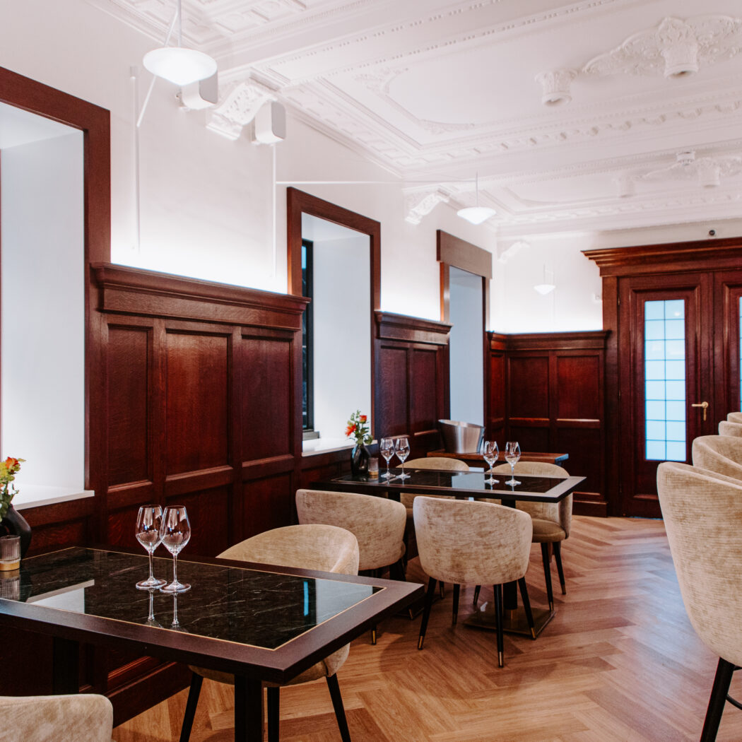 Sfeervol restaurantinterieur met donkerhouten lambrisering, marmeren tafels en een chef in een open keuken.