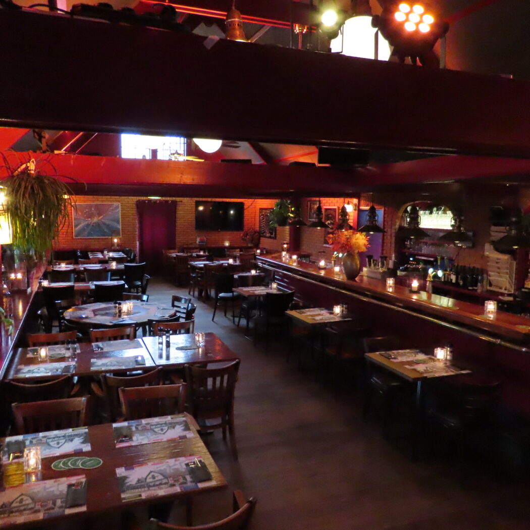 Warm verlicht restaurant interieur met rode bakstenen muren, eettafels en een lange bar met kaarsen.