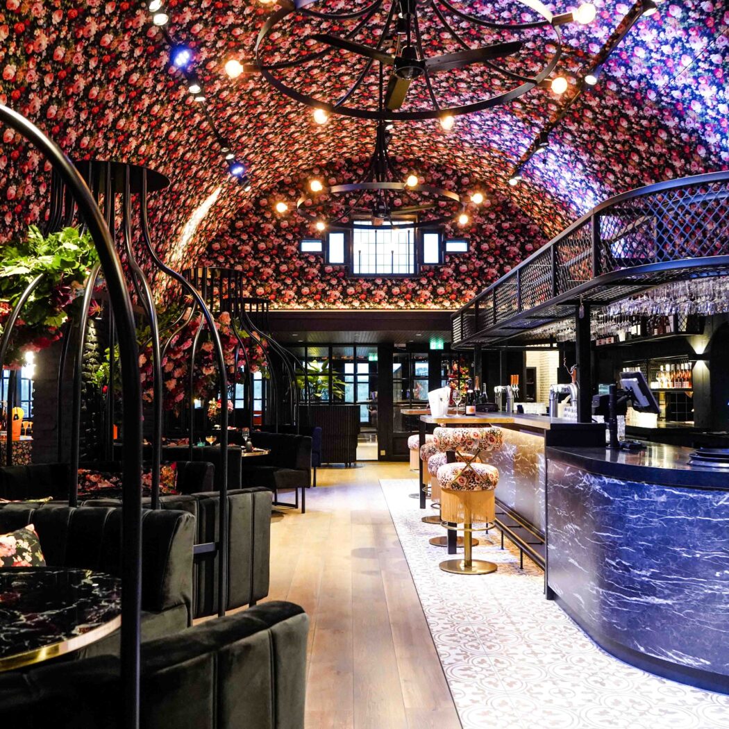 Luxe restaurantinterieur met rijkbloemig boogplafond, zwarte fluwelen banken en een donkerblauwe marmeren bar.