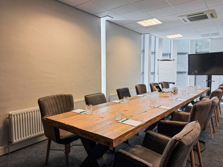 Een moderne vergaderruimte met lange houten tafel, gestoffeerde stoelen, een flipchart en groot tv-scherm.