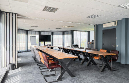 Stijlvolle vergaderruimte met lange houten tafels op metalen X-poten, diverse stoelen en groot scherm.