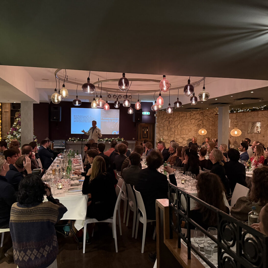 Gasten luisteren naar een spreker tijdens een presentatie-diner, met 7 moments that matter in 2024 op het scherm.