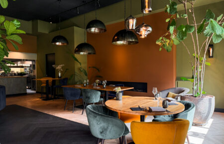 Sfeervol restaurant interieur met houten tafels, fluwelen stoelen in teal en mosterdgeel, en muren in olijfgroen en terracotta.